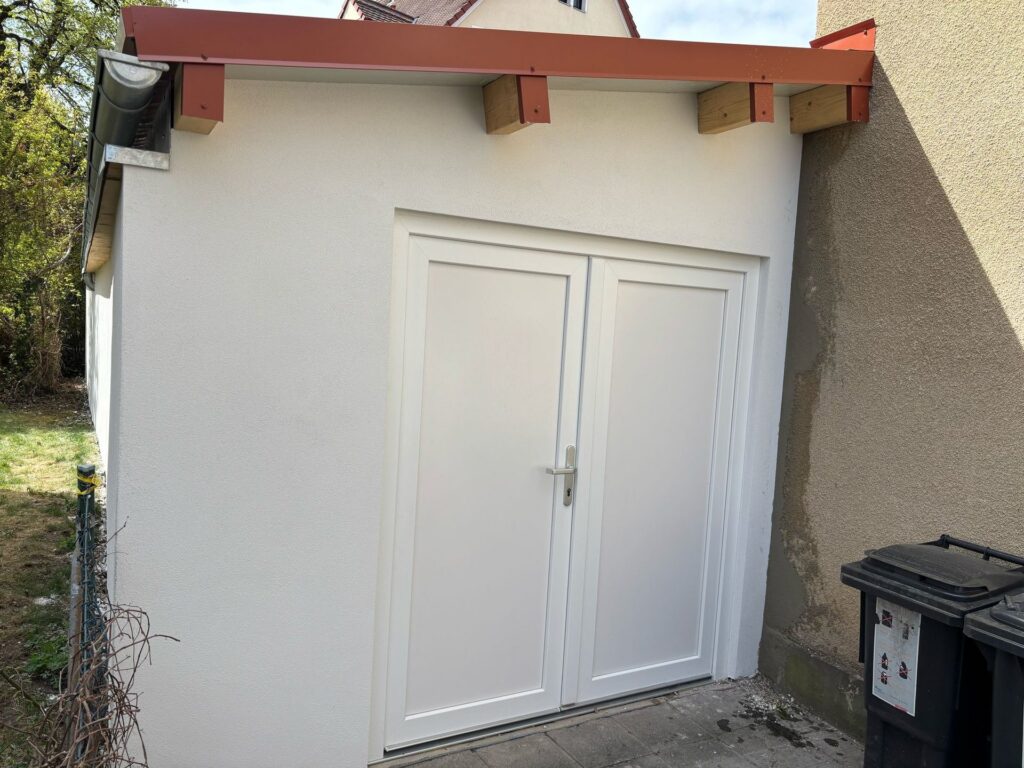 Fertige verputzte Garage mit weisser Tuer und rotem Dachrand