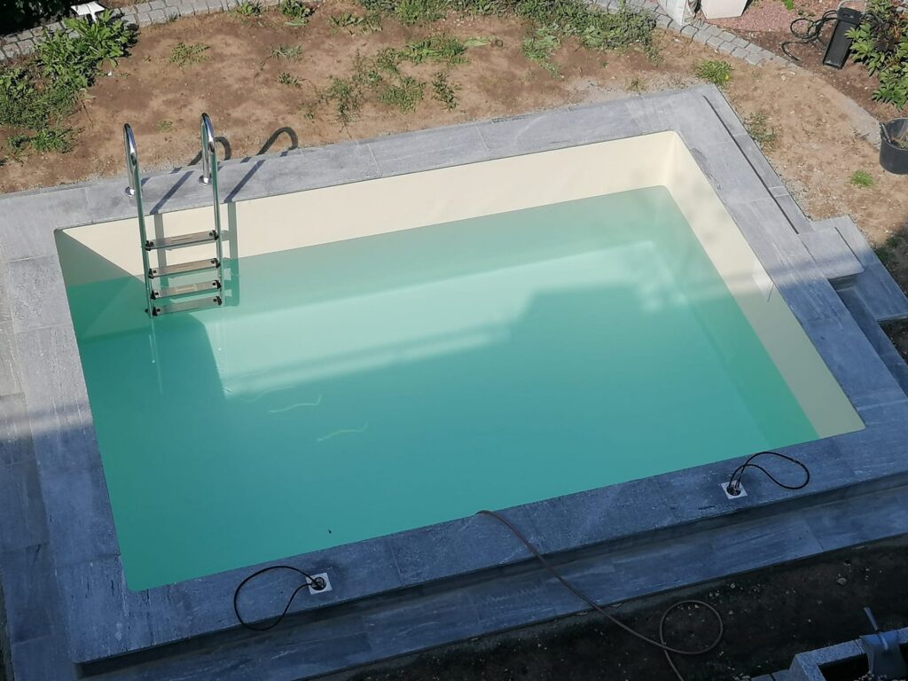 Fertiger Pool mit tuerkisem Wasser und Einstiegsleiter von oben